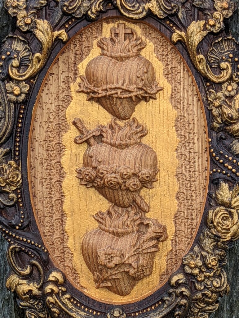 A wooden plaque depicting the hearts of Jesus, Mary, and Joseph.