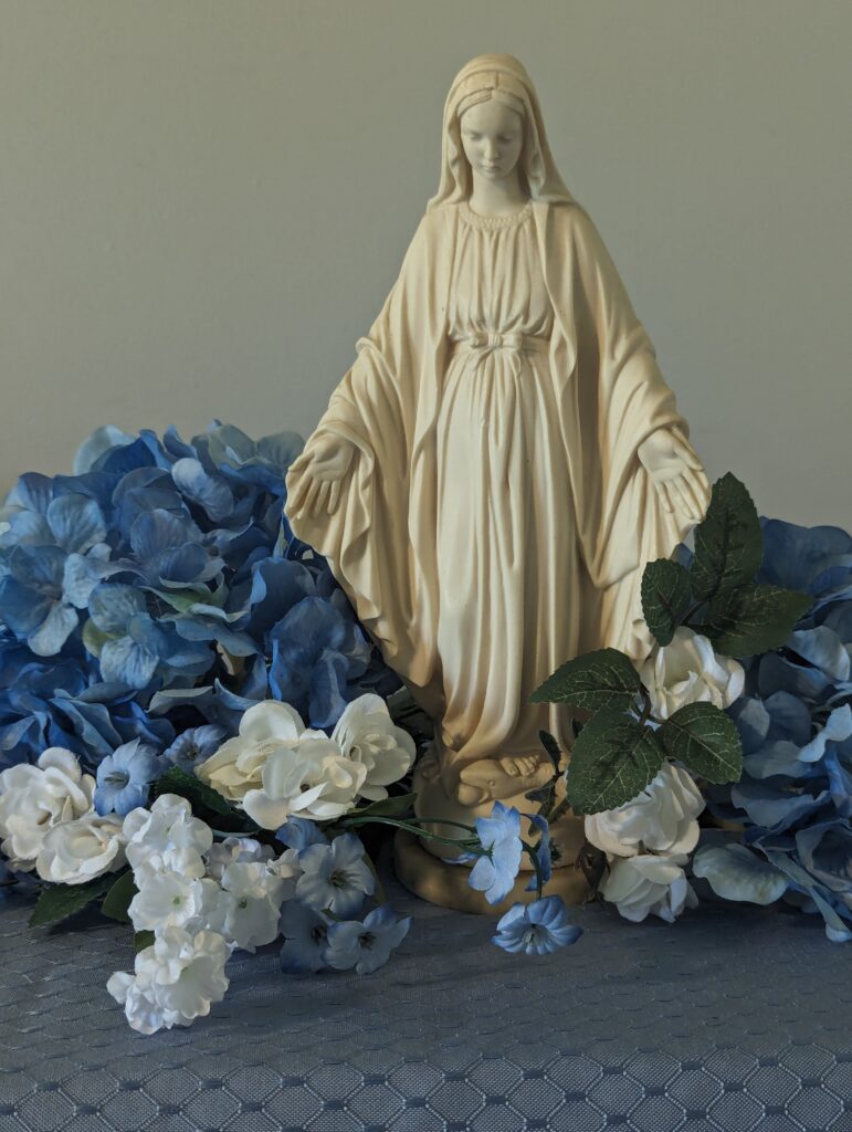 a statue of Our Lady surrounded by blue and white flowers on a blue cloth