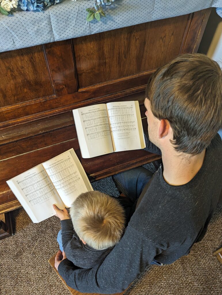 A boy and his father singing at home in front of a piano.
